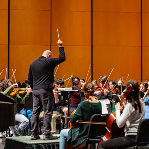 Conductor raising baton with musicians in front of him during a UW Symphony rehearsal. 