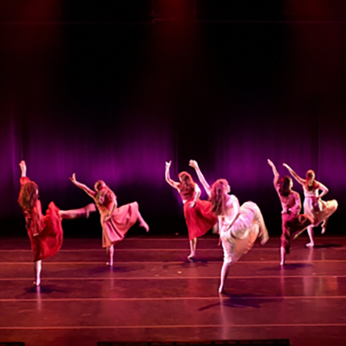 Six dancers lifting their leg in unison on stage.