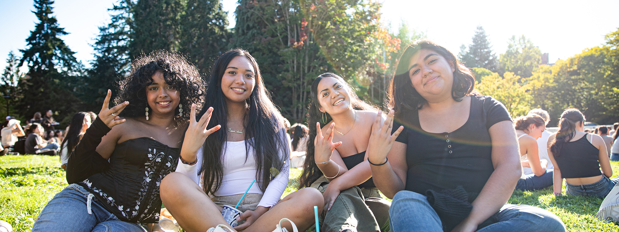 Four students sitting in quad, each making "W" sign with their fingers..