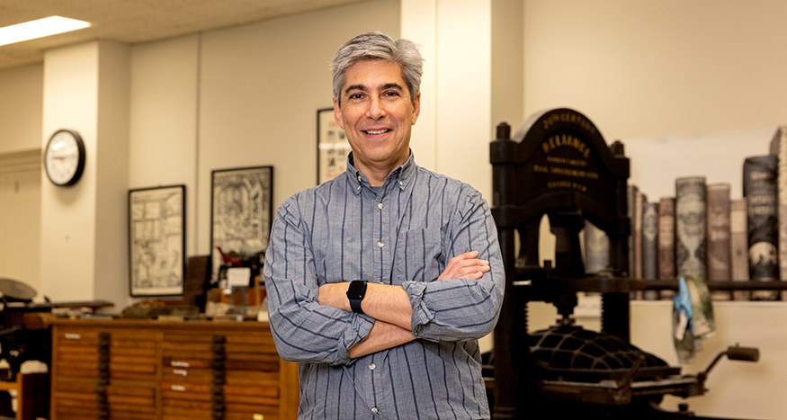 Geoffrey Turnovsky standing in front of a printing press in UW Special Collections. 