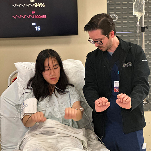 A neurology resident interacts with an actor who is in a hospital gown, role-playing as a neurology patient for a simulated training exercise.