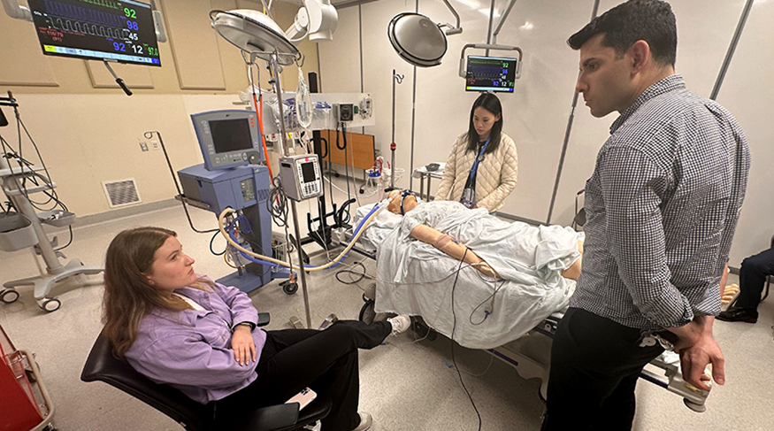 A neurology resident interacts with a family member as a patient is being examined nearby, as part of a simulated scenario..