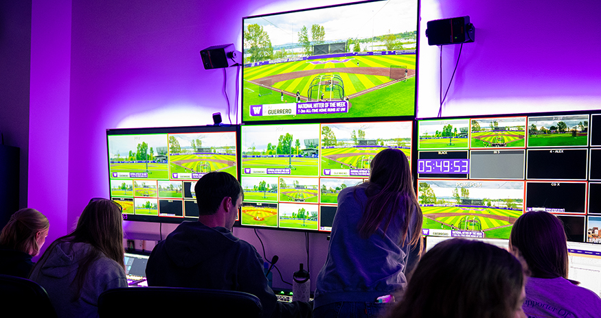 Students looking up at large screens in a broadcast control room.