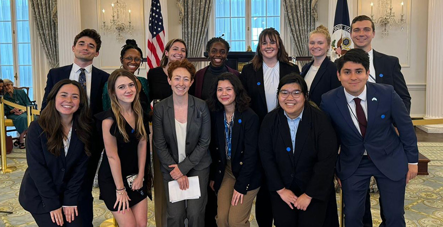 Grace Kelly and other State Department interns pose for a group photo with flags in the background.