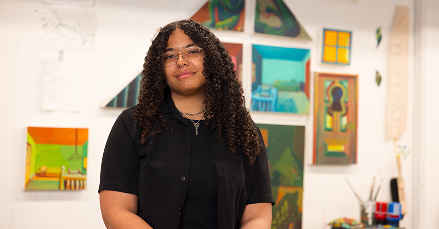 Kyra Wolfenbarger standing in front of her paintings in an art studio.