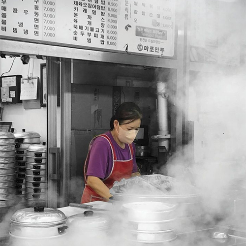 Steam rising from pots as a cook prepares dishes at a restaurant in Korea.