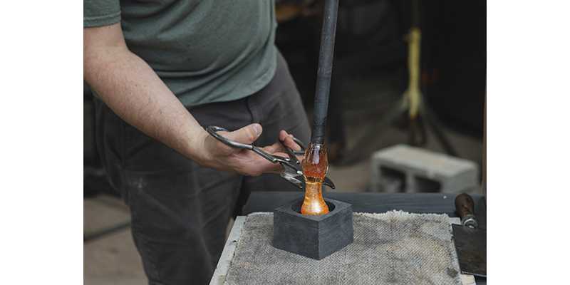 Hot glass is snipped from the end of a blowpipe, into a metal mold in the shape of a disk..