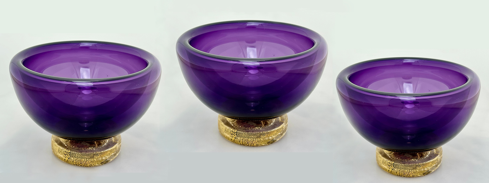 Three small purple blown glass bowls in a row. 