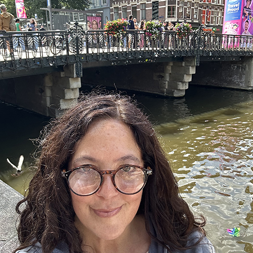 Ann Frost in Amsterdam, with a canal and bridge visible in the background.