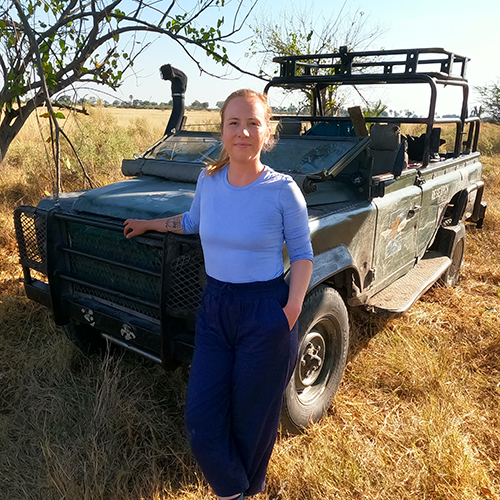 Researcher Leigh West in Botswana, standing beside a roofless car.