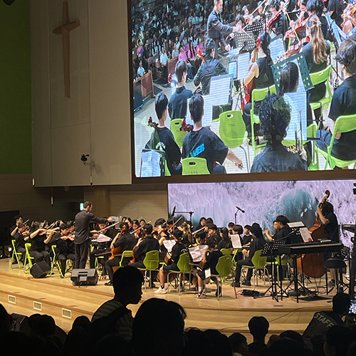 Federal Way Youth Symphony performing, with the performance projected on a large screen above them.
