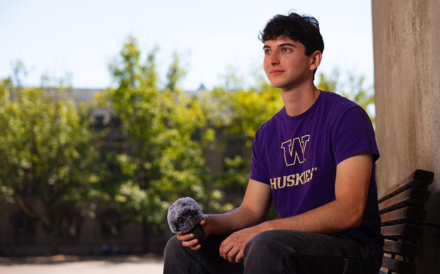 Leo Freedman sitting on a bench on campus, with a microphone in his hand.
