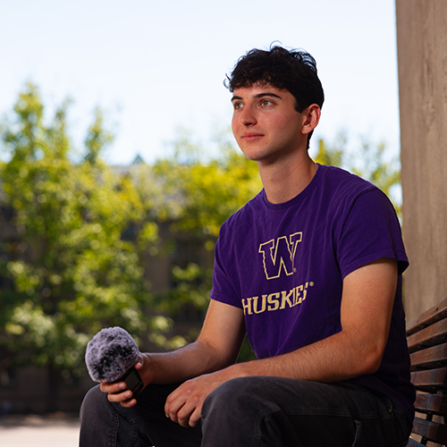 Leo Freedman sitting on a bench on campus, with a microphone in his hand.
