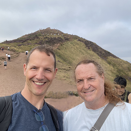 Scott Magelssen and Geoff Korf with people behind them hiking up a grassy hill.