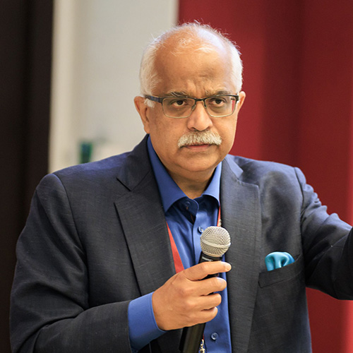 Aseem Prakash in a suit, holding a microphone