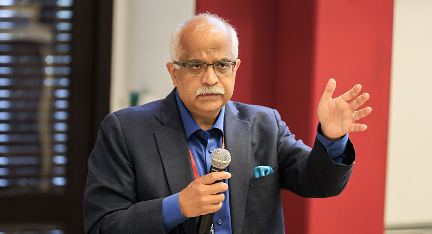 Aseem Prakash in a suit, holding a microphone