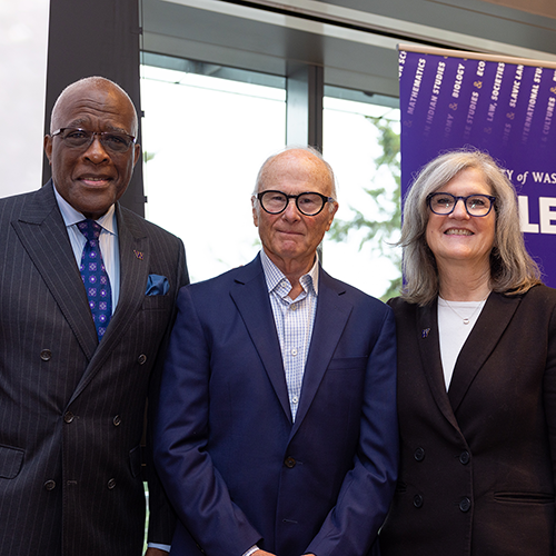 Three smiling people on stage in front of a College of Arts Sciences banner