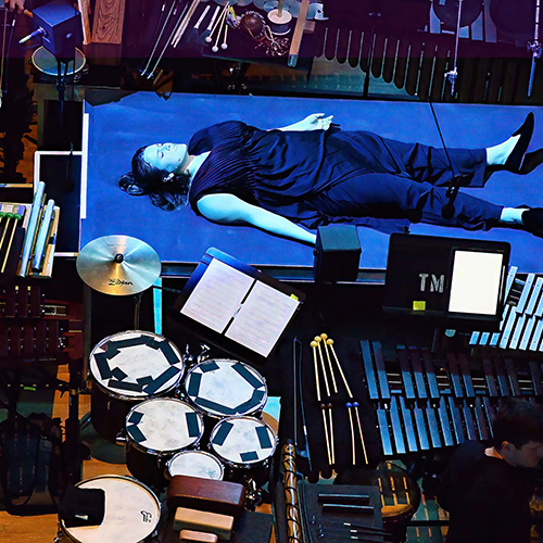 Detail from Music for New Bodies photo, showing someone laying down surrounded by percussion instruments.