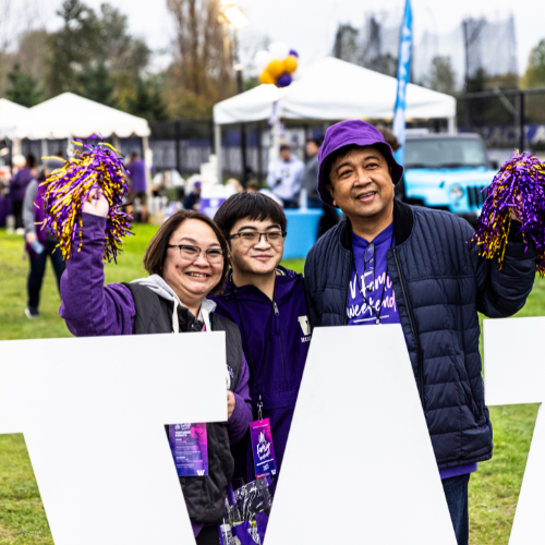 UW student with family members holding purple and gold pom poms behind a white "W" sign