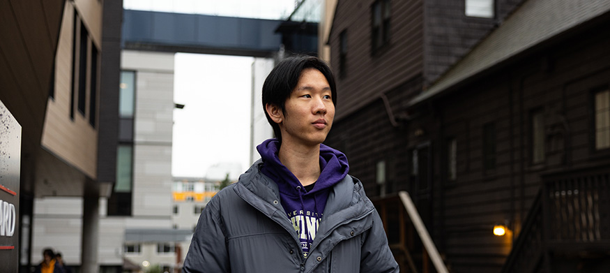 UW student Edwin Bai walking in Seattle's University District with buildings in the background,