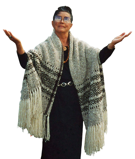 Vi Hilbert in a woven cape, with her hands raised.