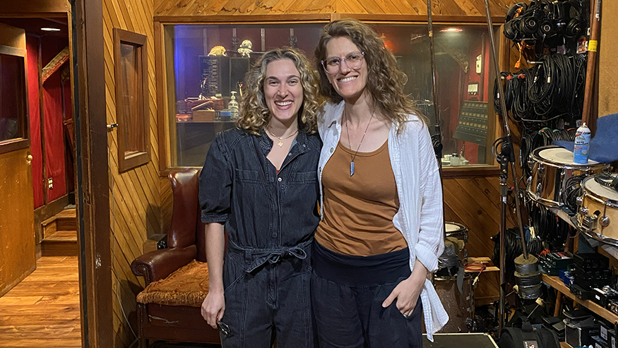 Andrea Roberts and Rocky Duval stand side-by-side in a recording studio, smiling at the camera.
