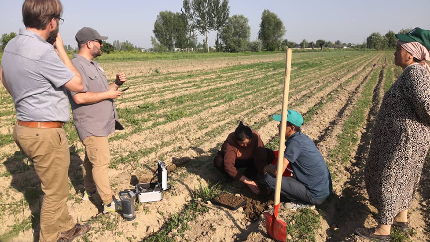 Jonathan Cox talks to farmers in a field with long rows of green crops stretching out behind them. 