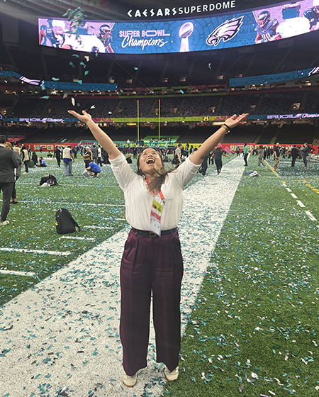 Thuc Nhi Nguyen raises her arms on the field at Caesars Superdome in New Orleans after the 2024 Super Bowl. 