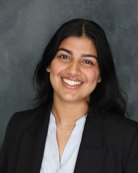 A smiling young woman in a suit posed in front of a marbled gray background.