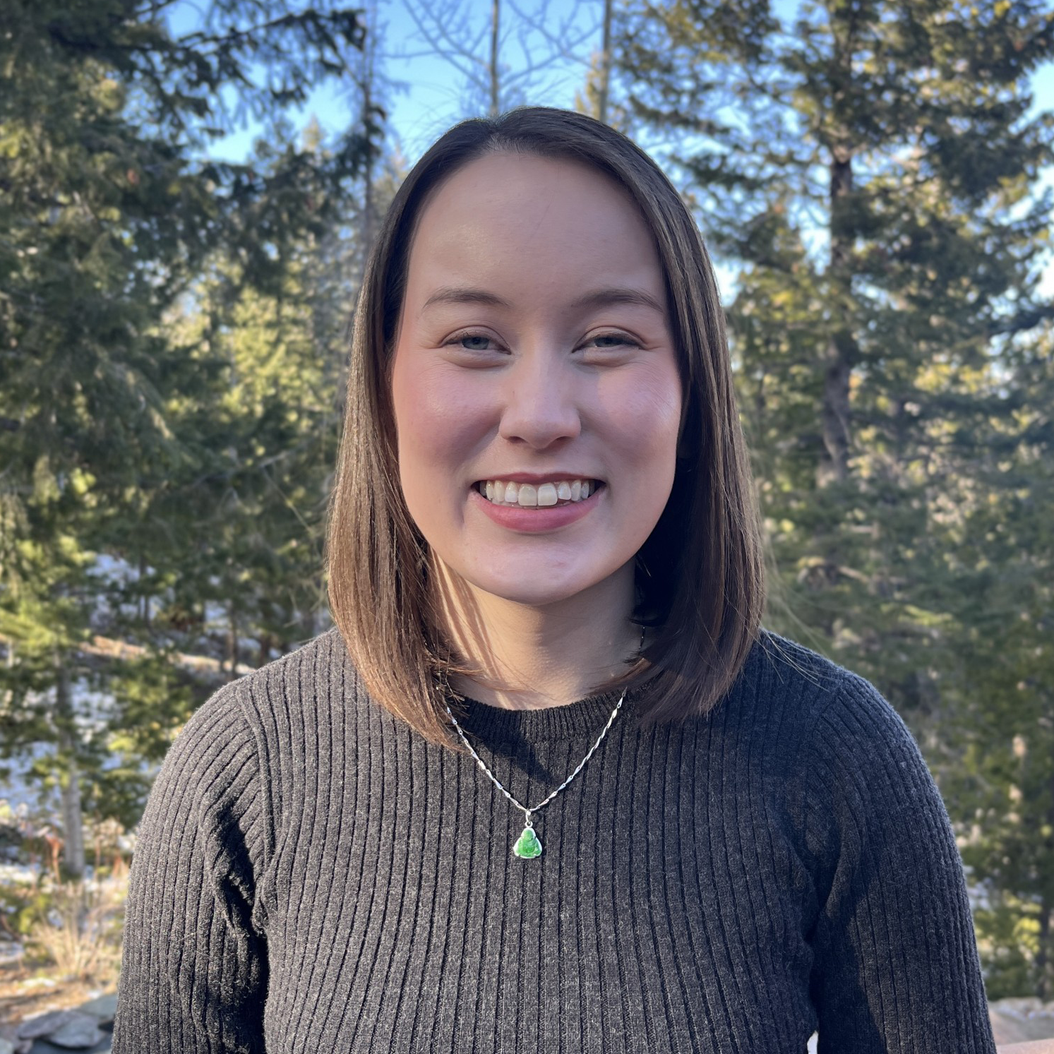 A smiling woman poses before an old growth forest.
