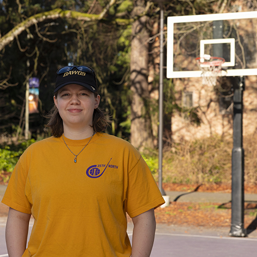 Maddy Brown in a t-shirt and baseball cap stands on a basketball court.