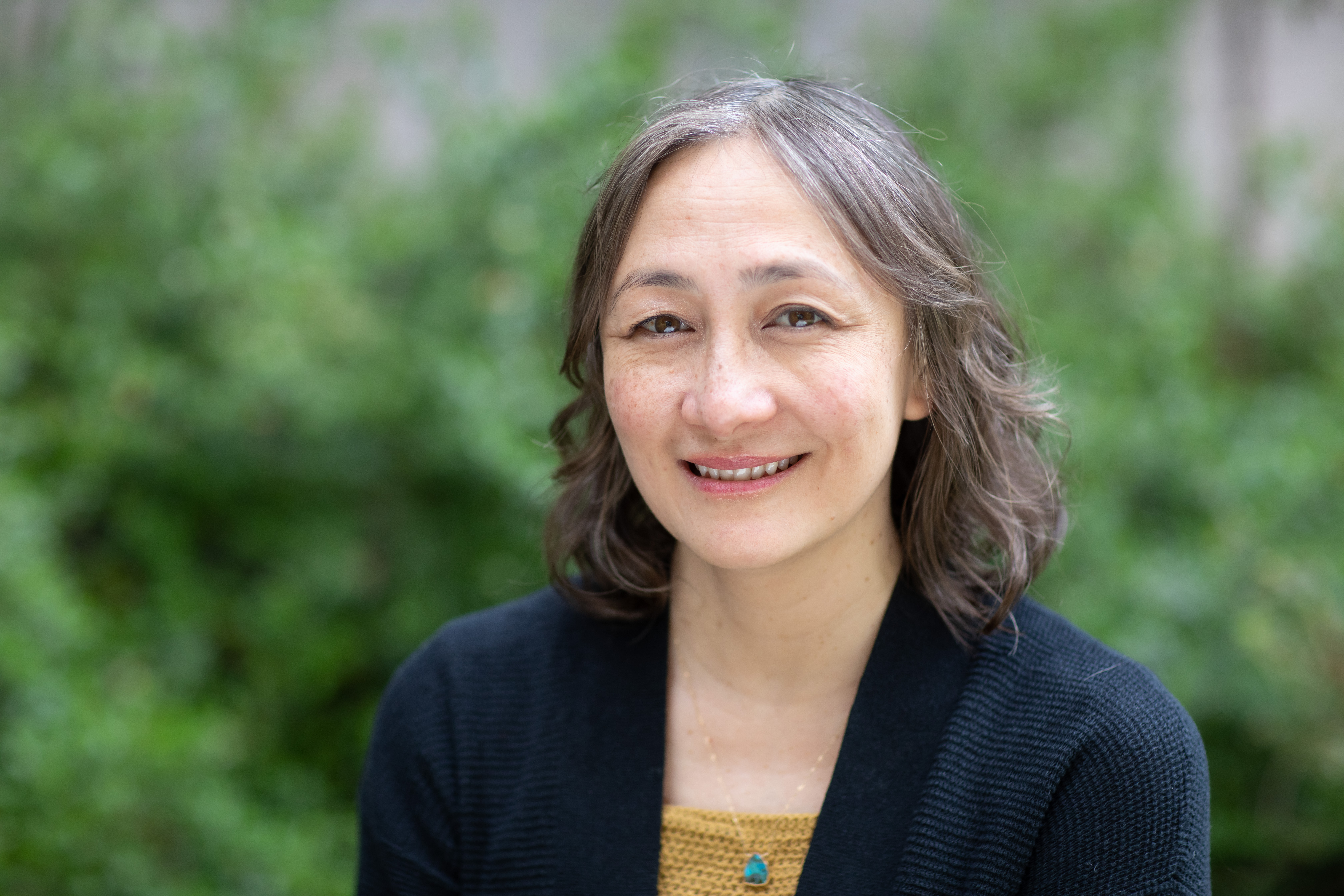 Candice Rai smiles in front of a lush green garden.
