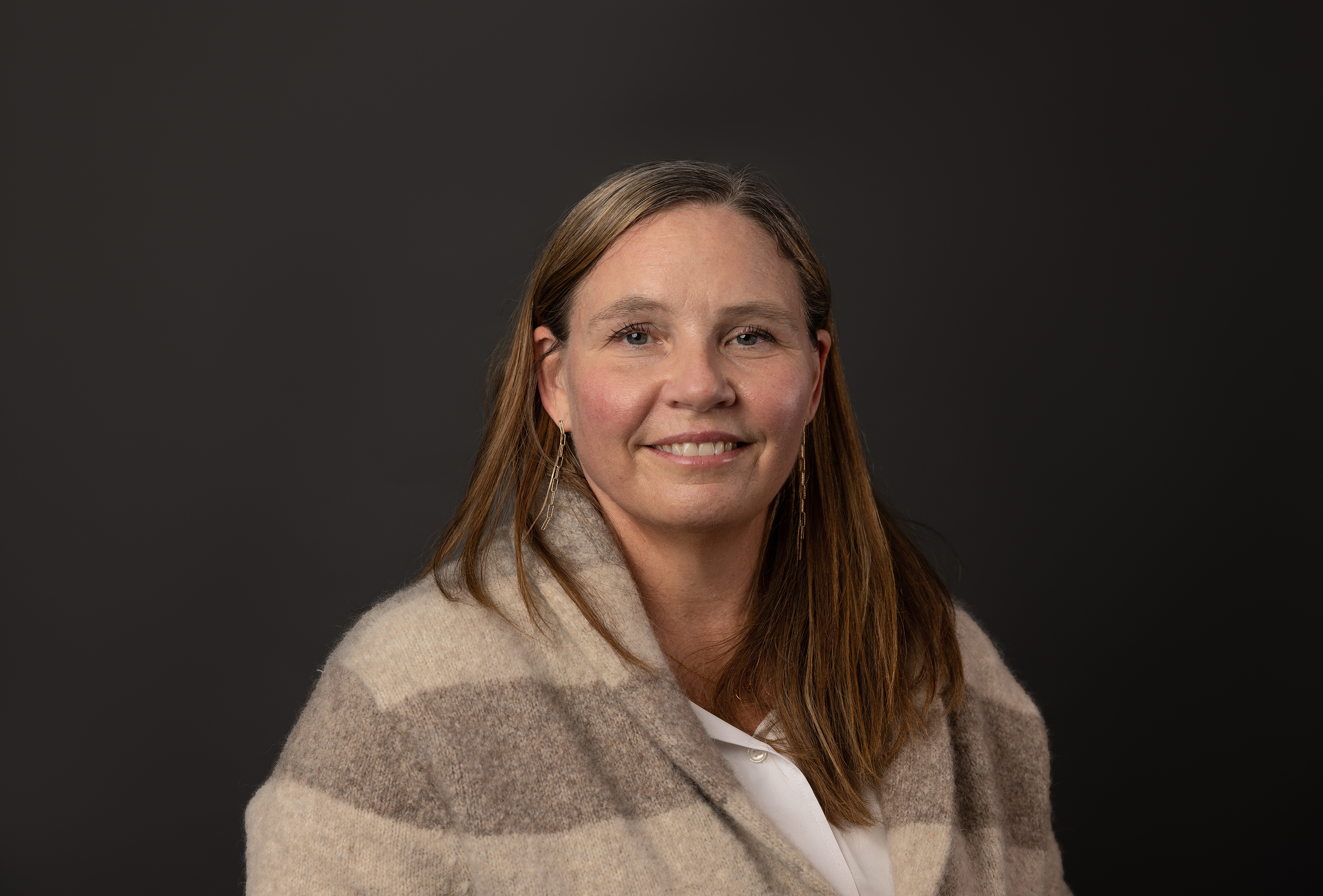 A woman in a brown striped shawl smiles.