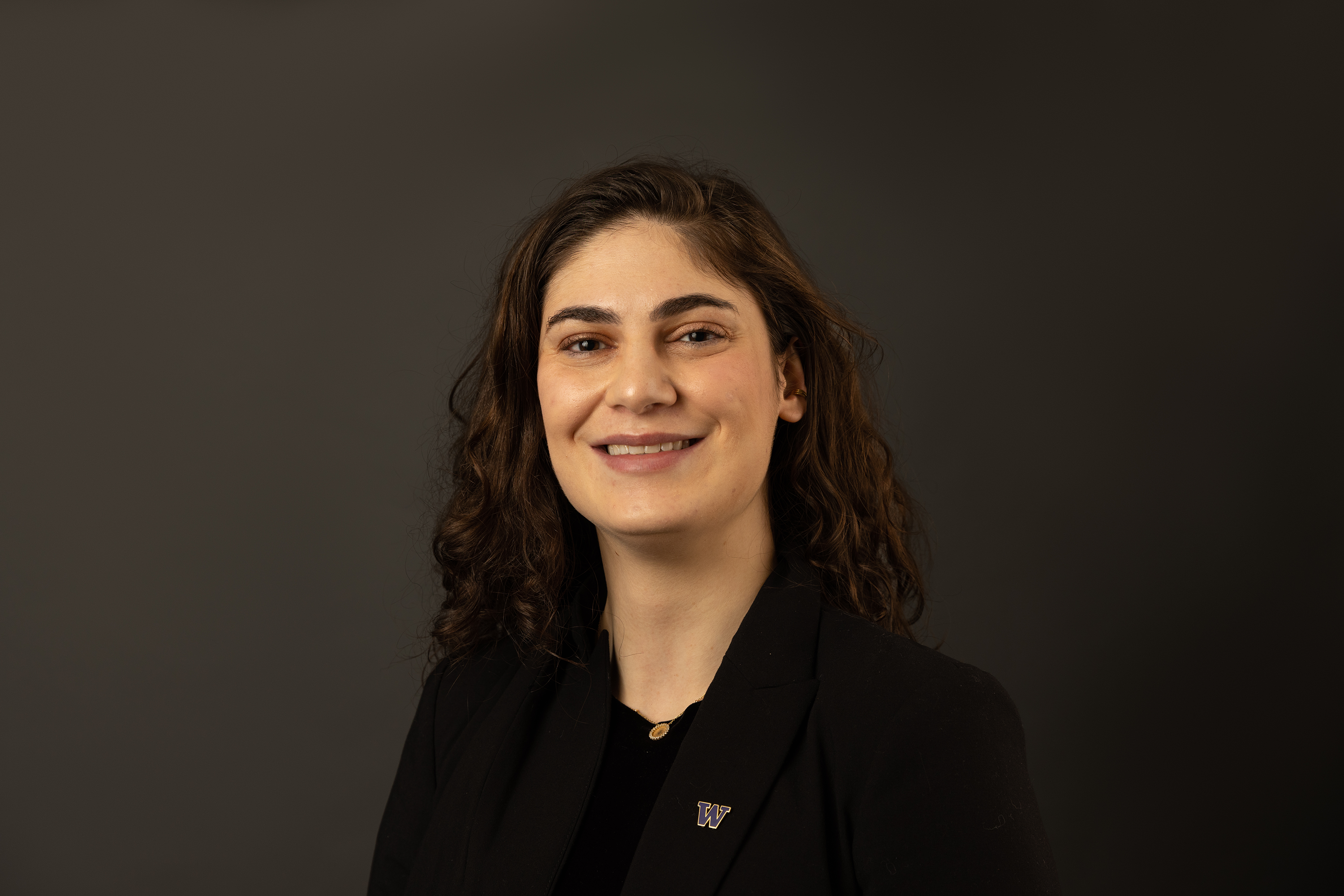 A woman with beautiful curly hair smiles. A pin in the shape of the letter W hangs from her black top.