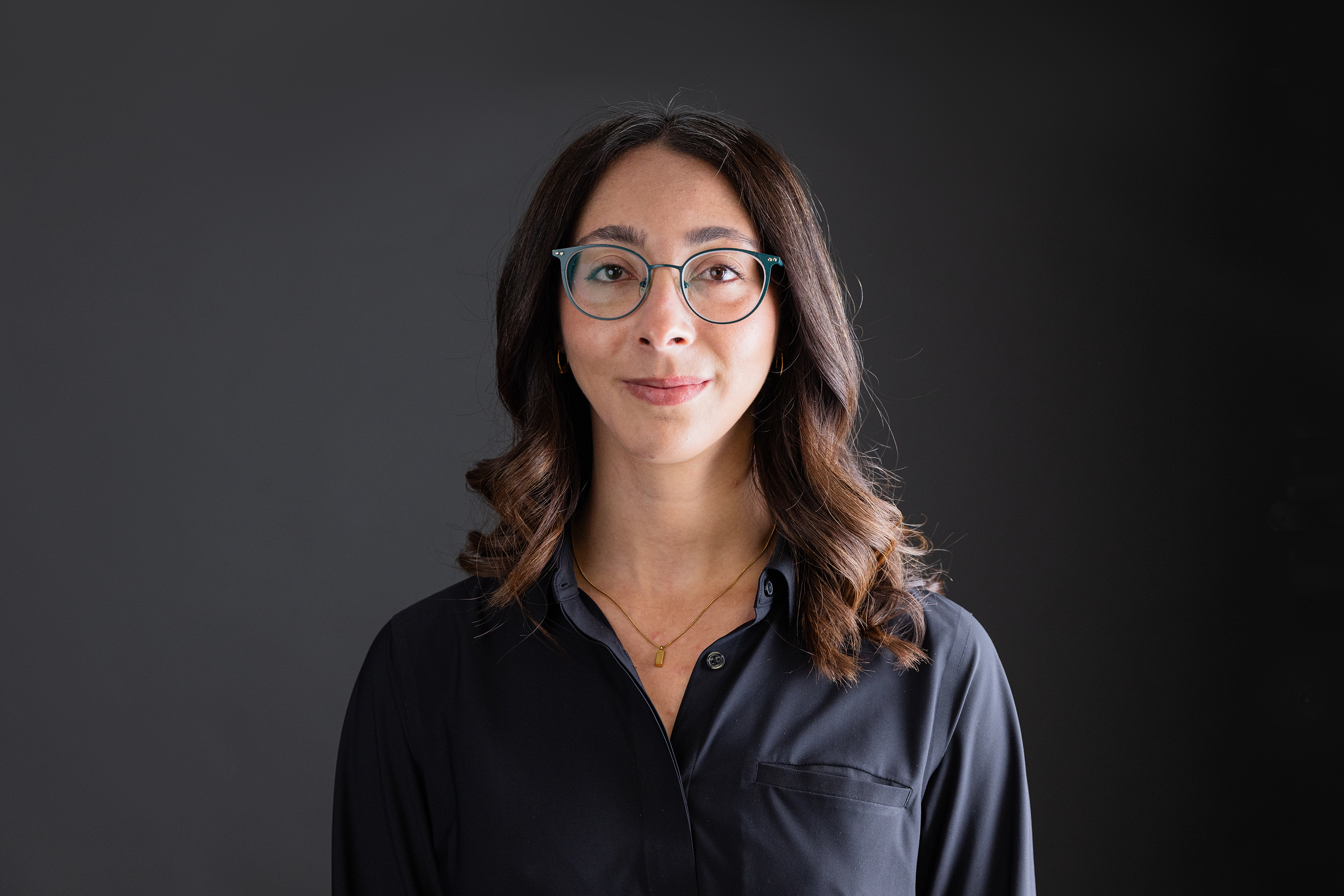 A woman with glasses and long dark hair smiles.