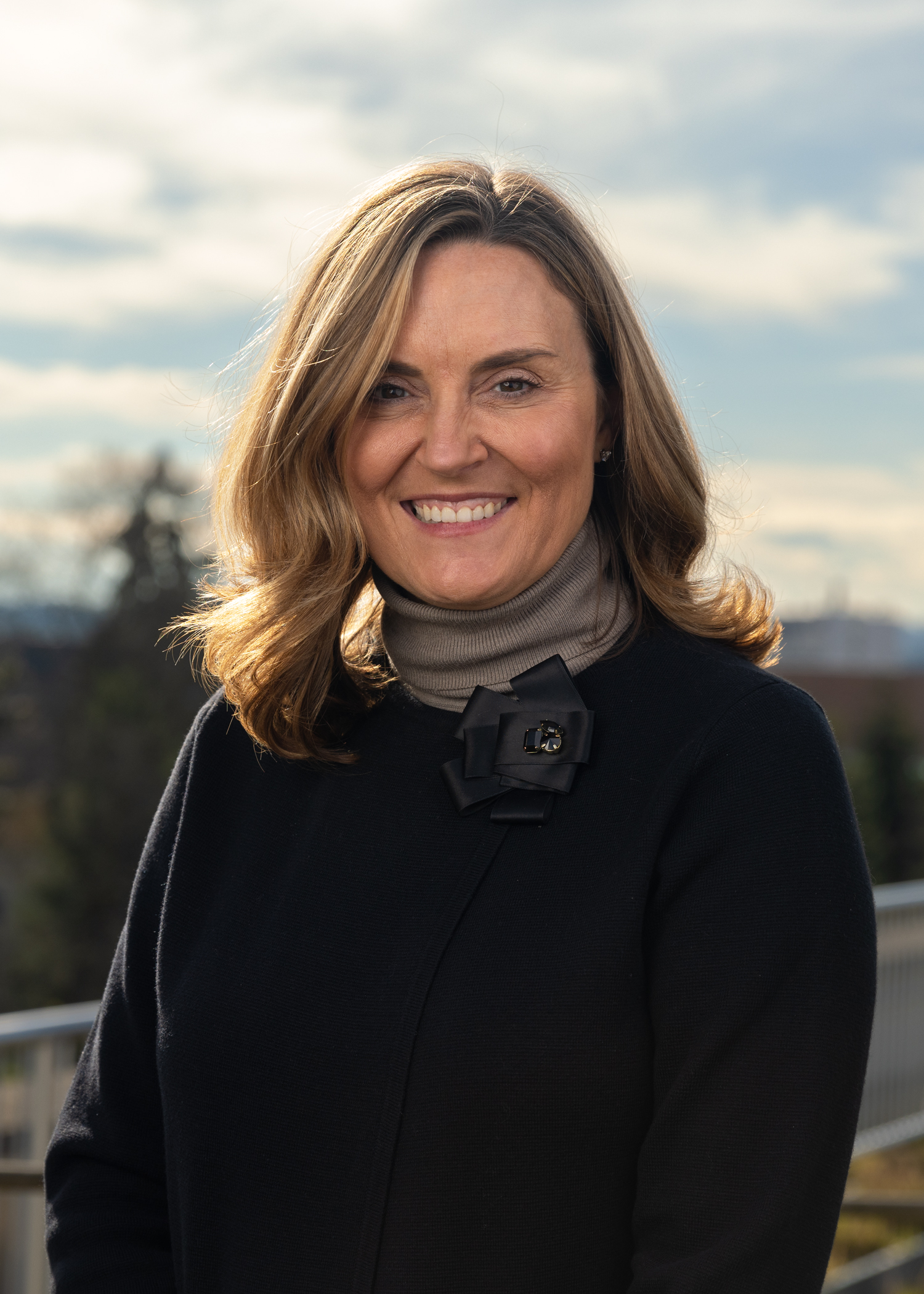 A smiling woman in a black jacket and brown cowl.