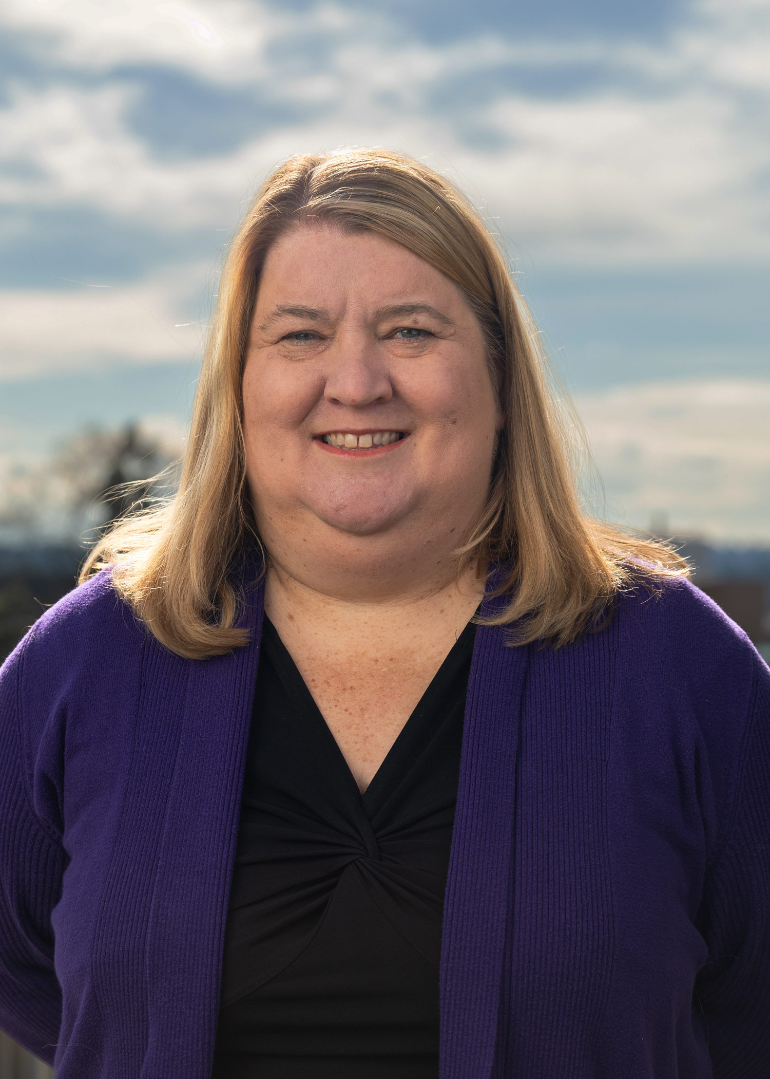 A smiling woman with blonde hair wearing a blue cardigan.