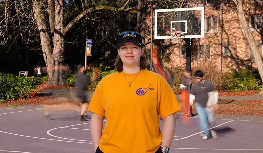 Maddy Brown in a t-shirt and baseball cap stands on a basketball court.