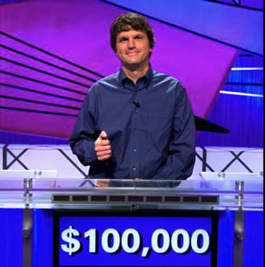 Tom Nissley holding the buzzer on the game show Jeopardy!, with the $100,000 on the front of his podium.