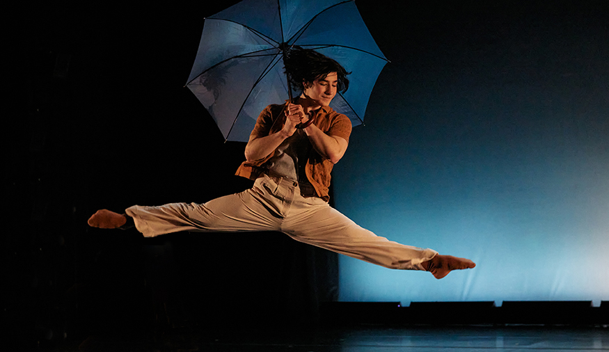 Eddie McClary leaping on stage while holding an umbrella, during a UW Dance performance. 