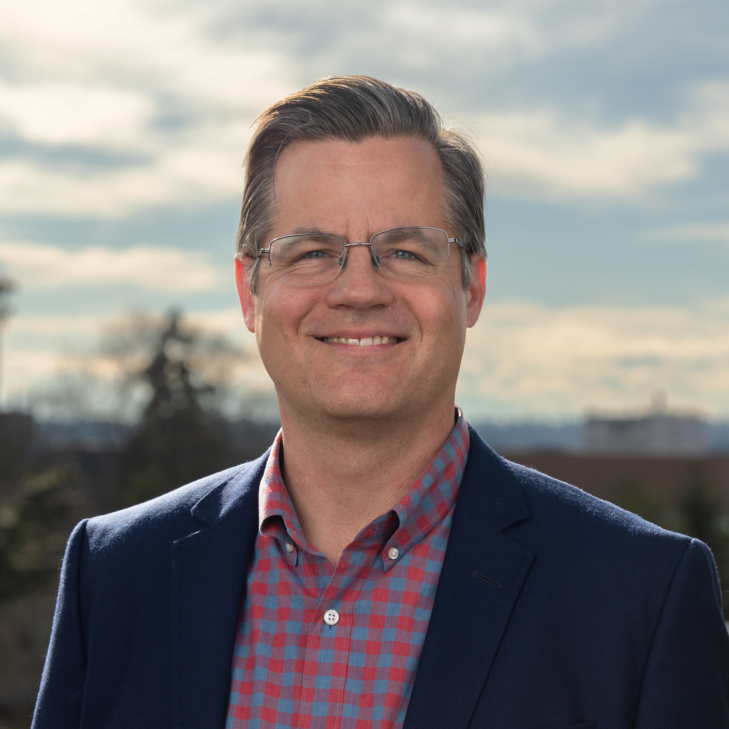 Dan Johnson smiles in front of a cloudy sky.