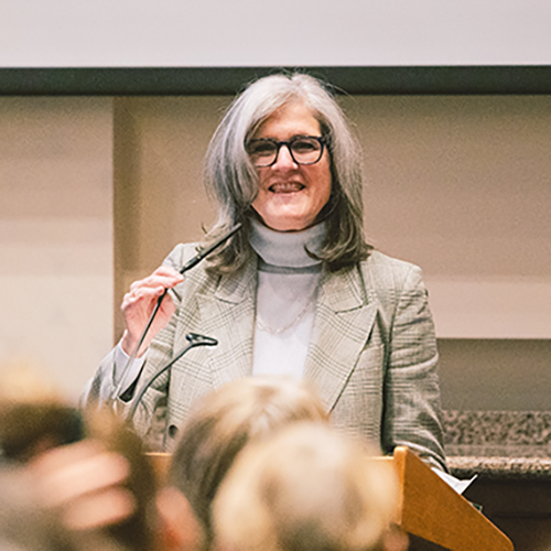 Dianne Harris holding a microphone, speaking to an audience.