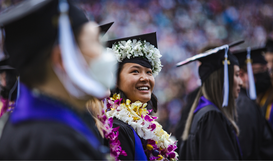 Class of 2024 graduates walking into the Husky Stadium during their Graduation Ceremony; a smiling female graduate is in focus