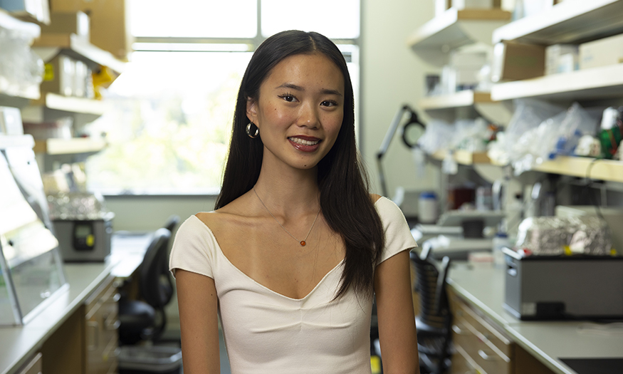 Hunter Jung in a research lab, with shelves of lab equipment on either side of her.