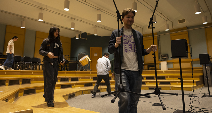 Students grad microphone stands in a performance space.
