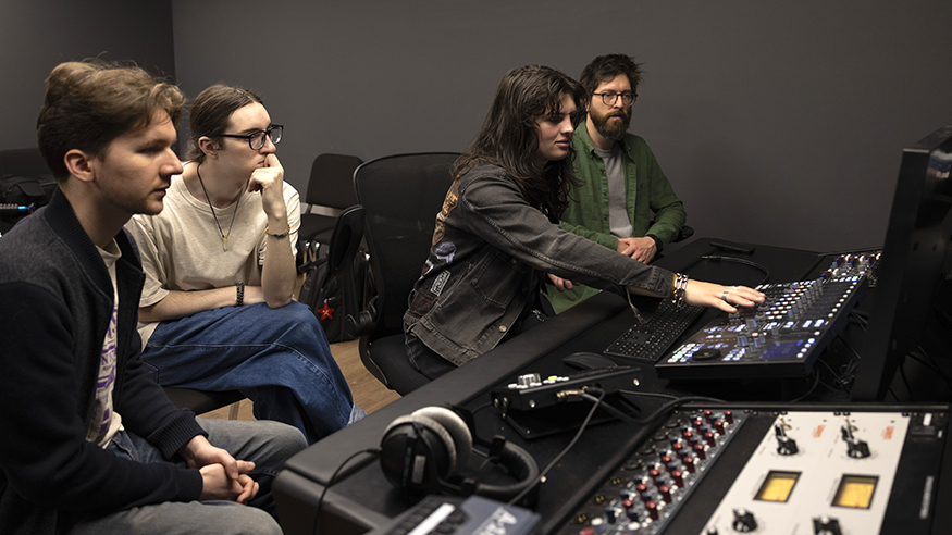 Four students work with recording equipment in the recording studio. 