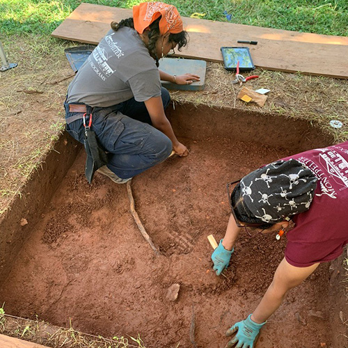 Two people excavating a shallow section at an archaeological site. 