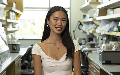 Hunter Jung in a research lab, with shelves of lab equipment on either side of her.