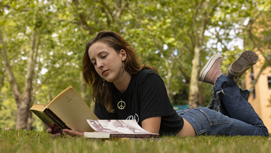 Piper Sorensen laying in the grass, reading an old paperback missing its cover.