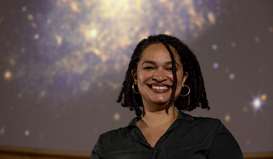 Arianna Long in the UW Planetarium, with galaxies projected on the screen overhead.